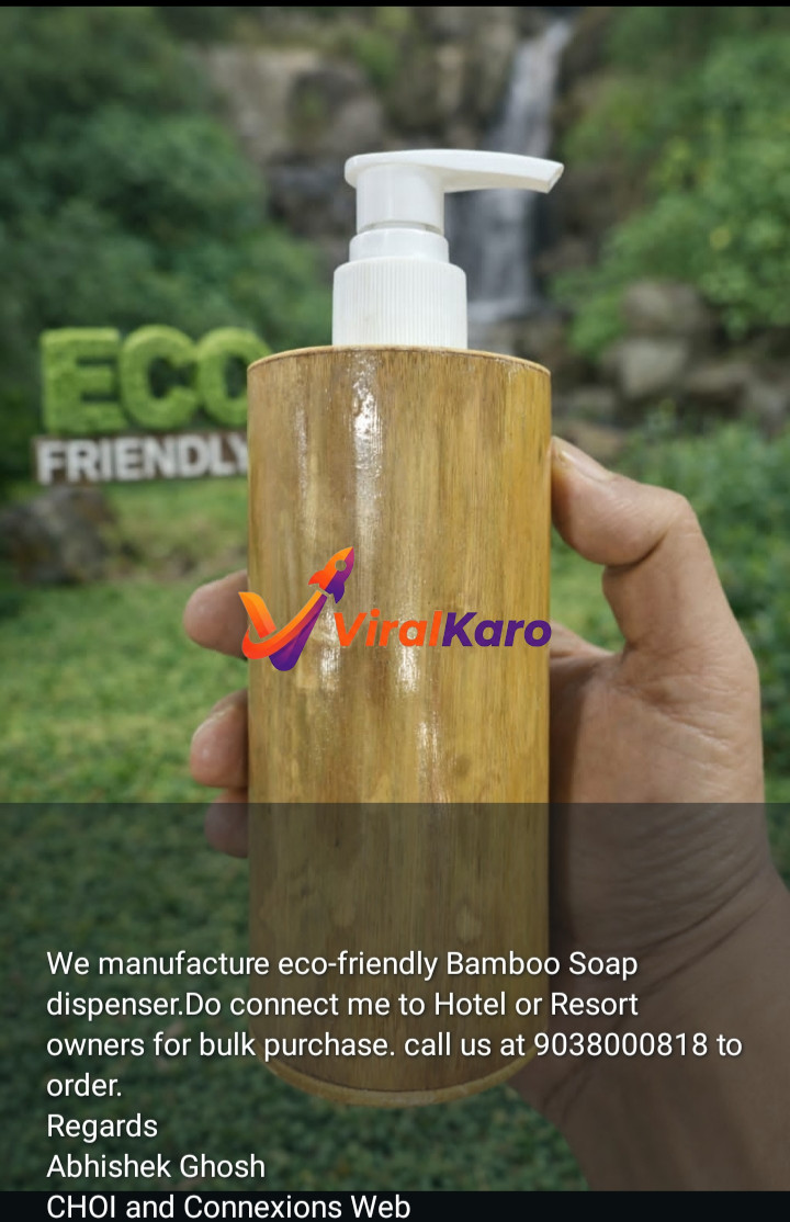 A hand holding a sleek, light brown bamboo soap dispenser with a white pump, set against a blurred background of lush green foliage and a natural waterfall. In the mid-ground, 'ECO FRIENDLY' text made of green grass is visible, emphasizing the product's sustainable nature. The image highlights the eco-conscious design of the bamboo dispenser, ideal for hotels and resorts seeking green amenities.